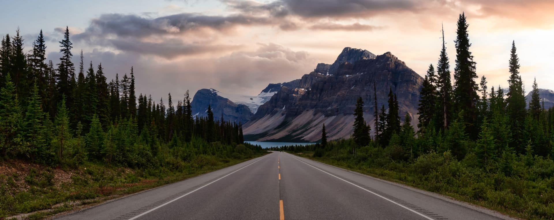 A scenic highway leading toward a mountain range and a lake