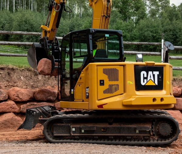 Excavator placing large red stones for a retaining wall