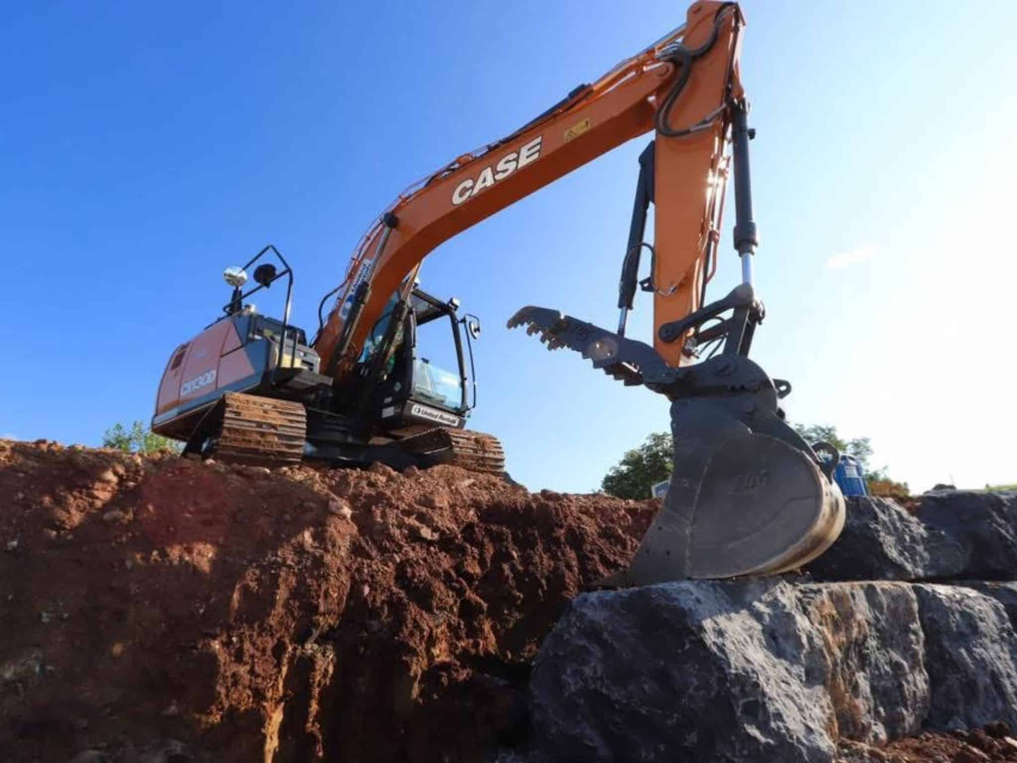 Excavator with a claw attachment placing large rocks for a retaining wall