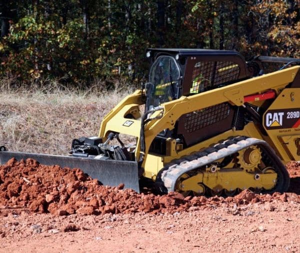 Compact track loader moving a pile of red dirt