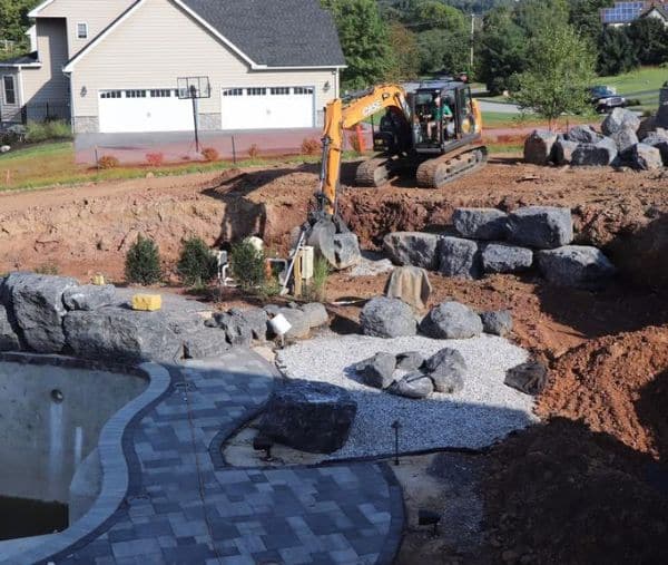 An excavator moving large rocks for a retaining wall and landscaping project